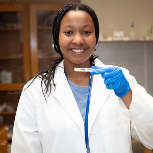 Portrait of Amari Griffis holding up a slide while wearing a lab coat